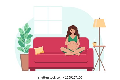 A pregnant woman is sitting on the sofa , smiling and hugging her big belly.