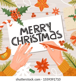 Preparing for New Year. Woman's hands signs a Christmas card. Toys, snowflake, leaves, flower, tree branch and lettering on wood background. Holiday decor concept, top view. Vector.