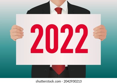 To present the balance sheet of his company, an executive in a suit and tie carries a white sign on which is written the year 2022.