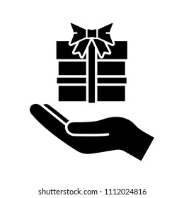 Present glyph icon. Silhouette symbol. Open hand with gift box. Giving, getting gift. Negative space. Vector isolated illustration