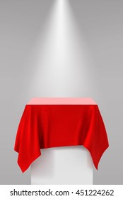 Presentation pedestal covered with a red silk cloth in front of a white wall illuminated by a spot light