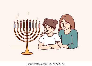 Preteen girls sisters look at menorah with burning candles and rejoice at approach of holiday of hanukkah. Menorah on table near two happy children symbolizes jewish religion and honoring traditions