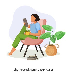 Pretty girl sitting in comfy armchair with a tablet and cup of coffee.