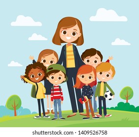 Pretty teacher standing with pupils in school yard. Classmates portrait with teacher on landscape background. Elementary school.