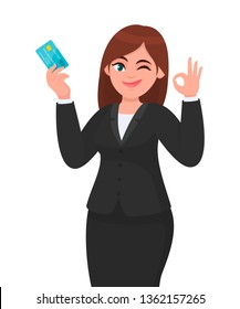 Professional business woman showing/holding credit/debit/ATM banking card and gesturing/making okay/ok sign, while winking eye. Good, like, deal, agree, positive concept in cartoon. Modern lifestyle.