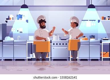 professional chefs couple preparing and tasting dishes african american woman man in uniform standing together near stove cooking food concept modern kitchen interior flat full length horizontal