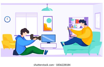 Professional photographer makes pictures of a guy sitting on the sofa with a laptop. Man with the camera takes pictures of the male freelancer. Shooting in apartment. A photo session at home