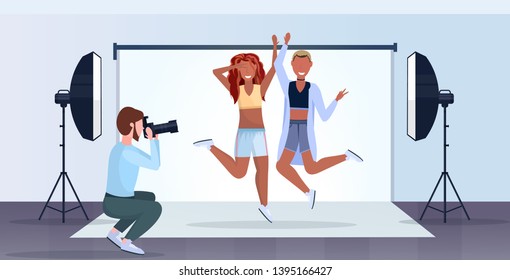 professional photographer using camera man shooting beautiful sexy african american women models posing and jumping modern photo studio interior horizontal full length