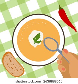 Pumpkin soup with sour cream and parsley. Someone is eating a tasty dish with a spoon. A plate with a delicacy on a tablecloth. A piece of bread and chili pepper