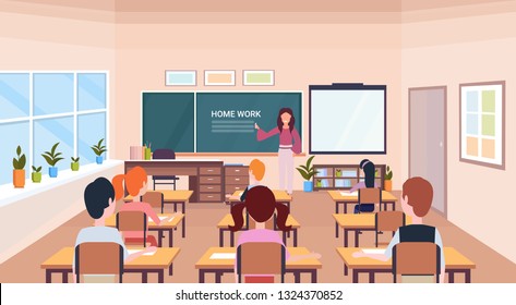 pupils looking at woman teacher writing home work chalk board modern school classroom interior horizontal flat