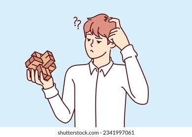 Puzzled man with puzzle toy scratches head and does not know how to solve assigned task. Dumb young male holding puzzle in hand and needs help due to low intelligence and IQ level.