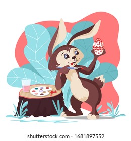 Rabbit artist enthusiastically draws Easter eggs. In a thicket of tall grass, on a stump are paints and a glass of water. Vector image in the style of a cartoon, on a white background. 