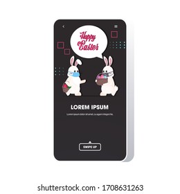 rabbits in medical masks holding baskets with eggs happy easter spring holiday coronavirus pandemic concept greeting card lettering smartphone screen mobile app vector illustration
