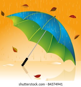 Rain and autumn leaves falling on a blue and green umbrella which is reflected on a glossy surface with water puddles