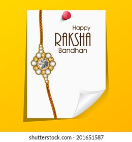 Rakhi with a paper note on bright yellow background on the occasion of Happy Raksha Bandhan. 