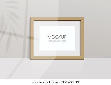 Realistic vector mockup with wooden photo frame. Shadow on the wall and empty place for your design. 3d soft light and overlay shadow from leaves of plant and window. Horizontal poster or painting.