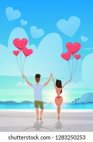 rear view couple holding pink heart shape air balloons sea ocean beach summer vacation concept man woman in love over sunset seascape background full length vertical flat
