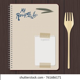 Recipe notebook graph with hand drawn text. Olive leaves and sheet of small notebook attached with adhesive tape. Wooden fork. Wooden background.