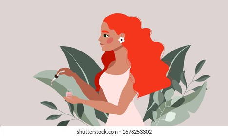 Red hair girl holding oil and pipette. Beautiful lady in a soft pink dress showing beauty product. Tropical leaves and tree branches. Floral earring. 