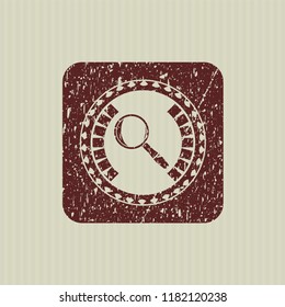 Red magnifying glass icon inside distressed rubber seal with grunge texture