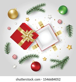The red opened gift box decorated the floor with pine leaves, Christmas balls, glass balls, stars and small pieces of golden paper on the gray floor to celebrate Christmas.