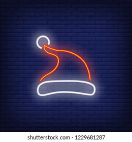 Red Santa hat neon sign. Glowing red cap on dark blue brick background. Can be used for winter, christmas time, festive