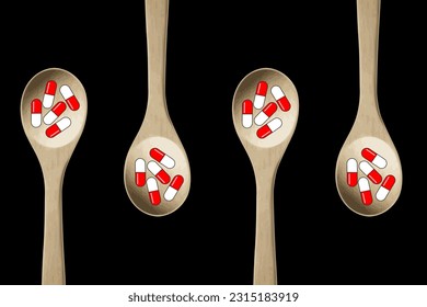 Red and white pills-capsules of medicines, vitamins or supplements in wooden kitchen spoons on black background. Concept of medicine and health