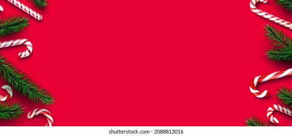 Red and white striped candy cane sticks with fir branches border. Red background. Space for text. Vector illustration.