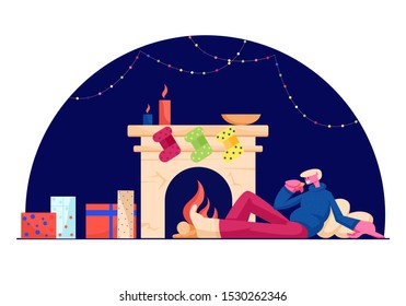 Relaxed Man in Warm Cozy Sweater Sitting on Pillows at Fireplace with Hanging Socks, Burning Candle and Many Gift Boxes Drinking Hot Beverage. Christmas Night Leisure. Cartoon Flat Vector Illustration
