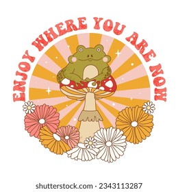 Retro 70s groovy funky frog with mushroom, flowers and sunburst. Enjoy where you are now slogan print with frog character sitting on mushroom. Naive groovy psychedelic vintage illustration. 