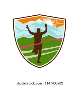 Retro style illustration of a silhouette of victorious marathon runner flashing victory hand sign with snow capped mountains and sunburst and finish line ribbon tape in shield or crest shape.