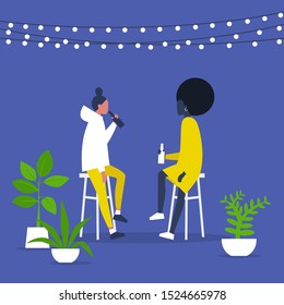 Romantic date in a garden: A couple of young adults drinking beverages on a terrace with string lights and plants