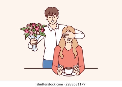 Romantic man with bouquet closes girlfriend eyes, wanting to make surprise and give favorite flowers. Romantic groom came on date with flowers for bride drinking coffee in cafe or bar 