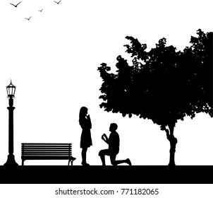 Romantic proposal in park under the tree of a man proposing to a woman while standing on one knee silhouettes