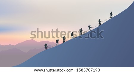 A roster of experienced alpinists climb the snowy slopes of a mountain to reach the summit. On the horizon the sun sets on the fairy landscape.