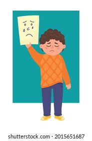 Sad boy holds piece of paper with drawn sad face. Emotional child development, empathy concepts.
