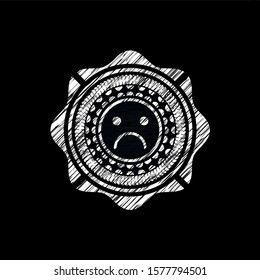 sad face icon inside chalkboard emblem on black board