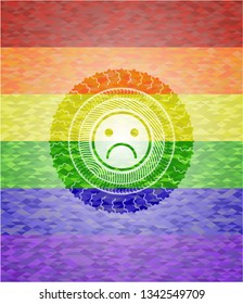 sad face icon inside emblem on mosaic background with the colors of the LGBT flag
