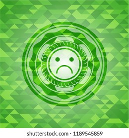sad face icon inside green emblem with triangle mosaic background