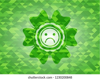 sad face icon inside green emblem with triangle mosaic background