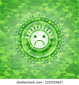 sad face icon inside green emblem with triangle mosaic background