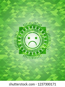 sad face icon inside green emblem. Mosaic background