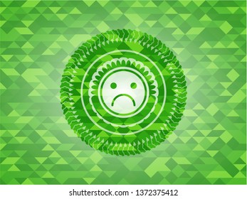 sad face icon inside green emblem. Mosaic background