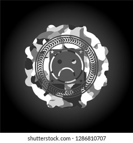sad face icon inside grey camouflaged emblem