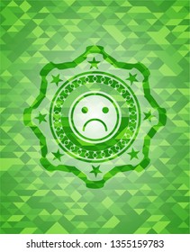 sad face icon inside realistic green emblem. Mosaic background