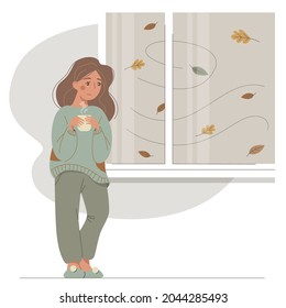 A sad girl in warm clothes stands by the window with a cup. Nice young woman warms her hands with a hot cup. Vector autumn mood illustration. 