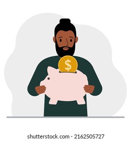 Sad man holds a piggy bank, a coin falls into the piggy bank. The concept of saving finance, savings, investing finances.