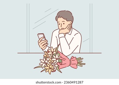 Sad man is waiting for girlfriend who is late for date, sitting in cafe at table with bouquet of flowers and mobile phone. Lonely guy is upset about getting rejected by girl to go on date together