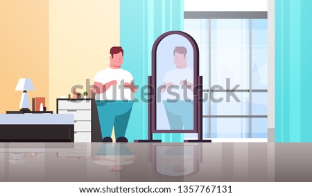 sad overweight man looking at himself reflection in mirror guy over size obesity concept modern apartment bedroom interior flat full length horizontal