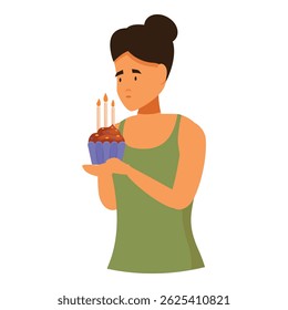 Sad pensive young woman holding birthday cupcake with burning candles making wish celebrating alone